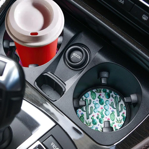 Cactus-pattern coaster fitted inside a car cup holder beside a red takeaway coffee cup