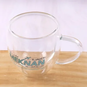 Clear glass mug with a printed green logo and transparent handle on a wooden surface