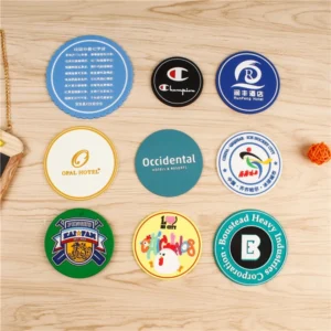 Nine round coasters with different printed logo designs arranged on a wooden surface