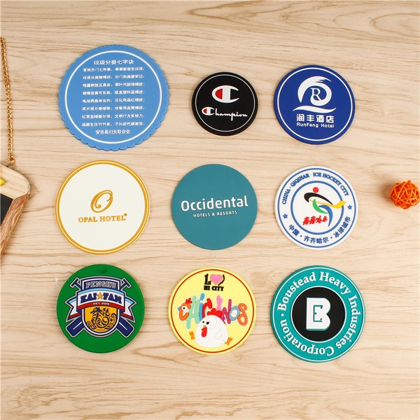 Nine round coasters with different printed logo designs arranged on a wooden surface
