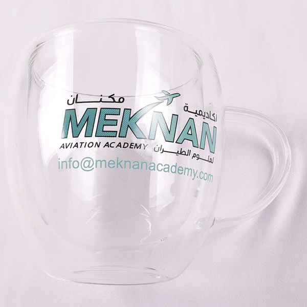 Clear handled glass mug with a green printed logo viewed from the front