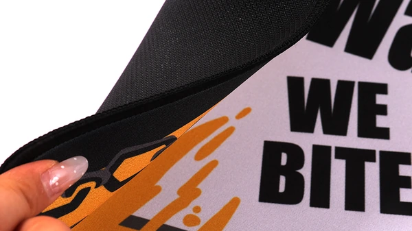 Hand bending a printed desk mat to show its edge and black reverse surface