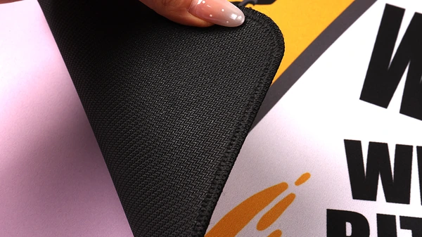Hand lifting a printed desk mat corner to show its textured black backing