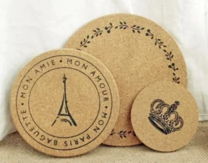 Three differently sized round cork coasters with Eiffel Tower, leafy border and crown designs