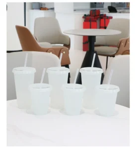 White tumblers with lids and straws arranged in several sizes on a table