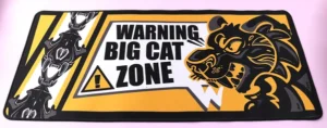 Rectangular yellow and black desk mat with a big cat illustration and warning text
